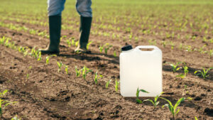 Herbicide jug container in corn seedling field, farmer walking in background,s elective focus